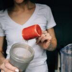a woman adding a scoop of protein powder into a shaker